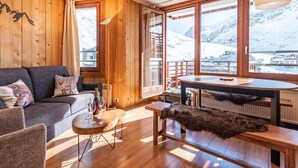 Ein gemütliches Zimmer mit Holzvertäfelung, einer Couch, einem Tisch und Blick auf einen verschneiten Berg.