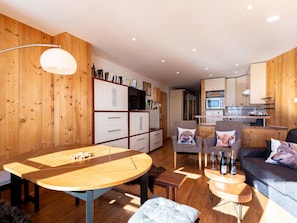 A cozy living area with a wooden floor, a round wooden table, two armchairs, a sofa, and a kitchen area with cabinets and a microwave. - Lovely apartment for 8 people with WIFI, TV and balcony (Les Boisses)