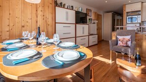 Eine moderne Küche mit Holzausbau, einem Esstisch für sechs Personen und einer gemütlichen Sitzecke mit Sessel und Kissen.