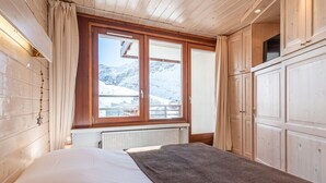 Ein Schlafzimmer mit großem Fenster, Holzwänden, Heizkörper und einem Bett mit brauner Decke.