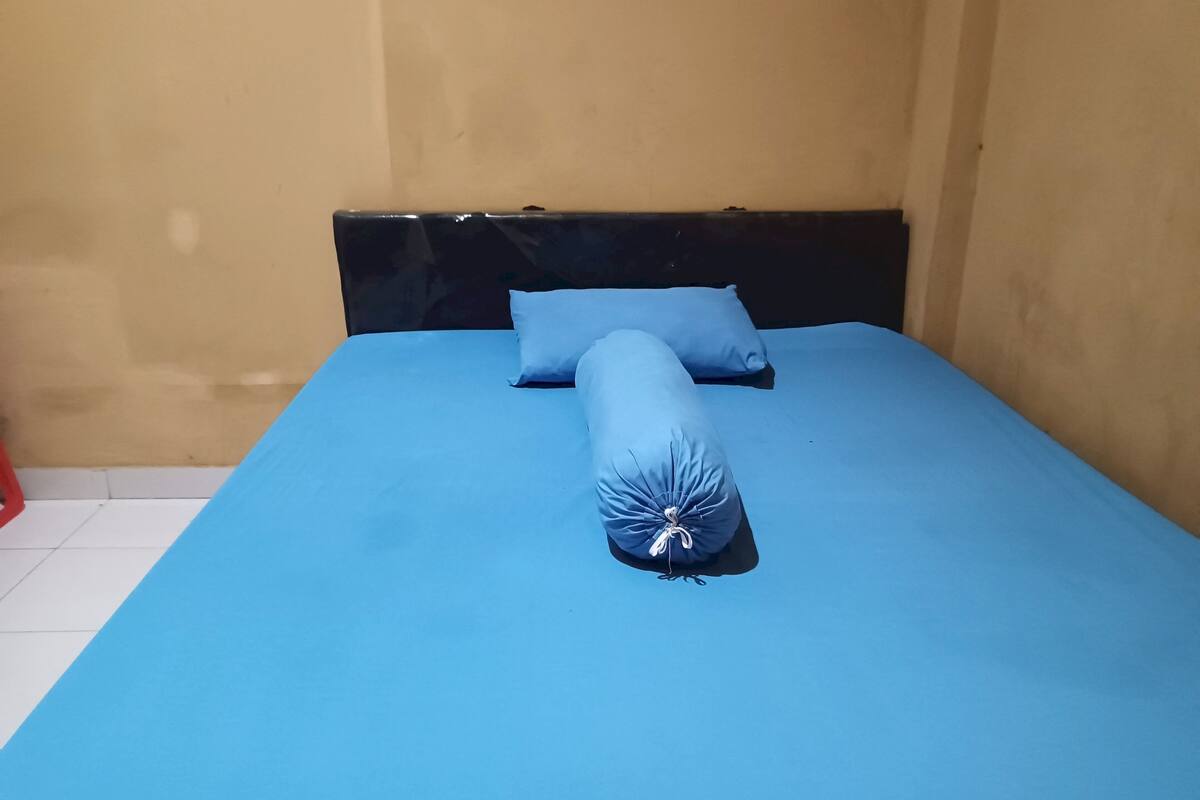 Een bed met een blauwe matras en kussens, een zwart hoofdbord en een betegelde vloer.