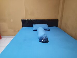 Uma cama com colchão e travesseiros azuis, cabeceira preta e chão de azulejos.