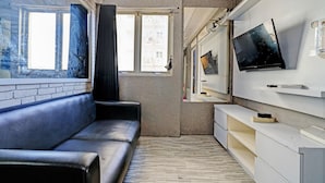 Ein modernes Wohnzimmer mit einer schwarzen Ledersofa, einem flachbildfernseher an der Wand und einem großen Fenster mit Vorhängen.