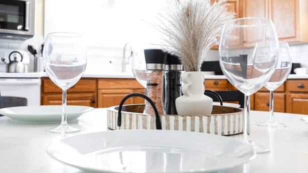 Una cocina con armarios de madera, encimera blanca y zona de comedor con una mesa dispuesta para dos.
