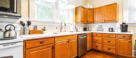 A kitchen with wooden cabinets, a stainless steel stove, a dishwasher, and a window with blinds.