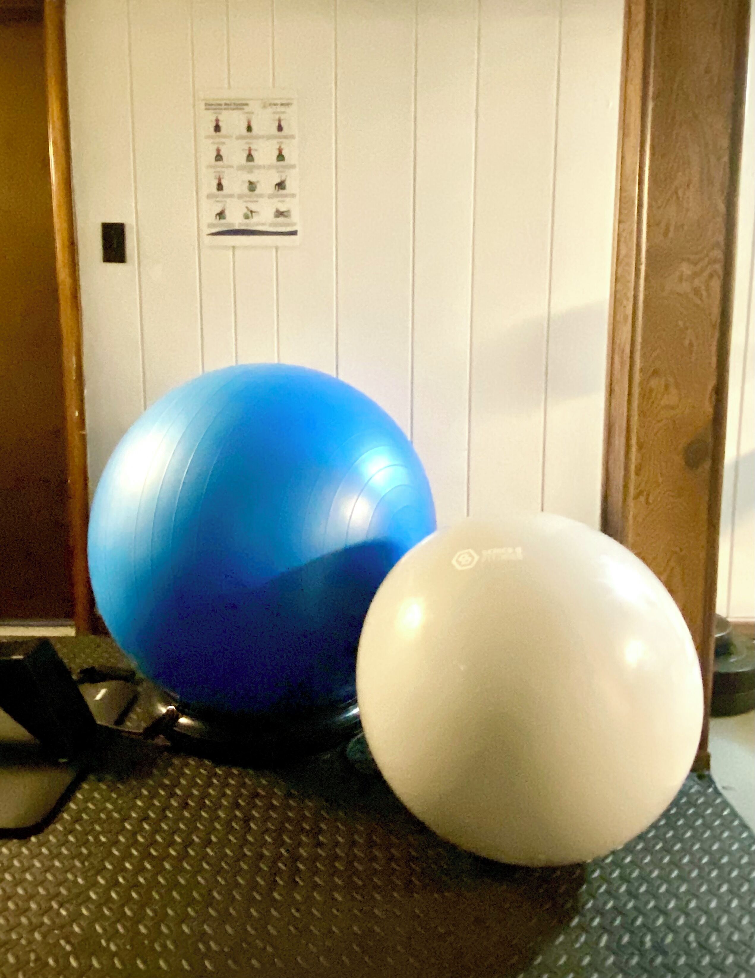 Twee trainingsballen, een zwarte mat en een muur met een deur.