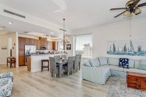 Una cocina moderna con armarios de madera, un comedor con sillas de mimbre, un sofá de color claro y un ventilador de techo.