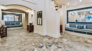 Un vestíbulo amplio con techo alto, una zona de estar con un banco de azulejos azules y blancos, y un espejo grande que refleja la habitación.