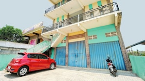 A multi-story building with a red car parked in front and a motorcycle to the right. - OYO Life 93075 Nova Jaya 2 Homestay Syariah (Paciran)