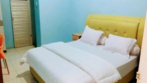 A neatly made bed with a yellow headboard and white bedding in a room with light blue walls. - Hotel O Home Stay Kembar Syariah (Binjai)