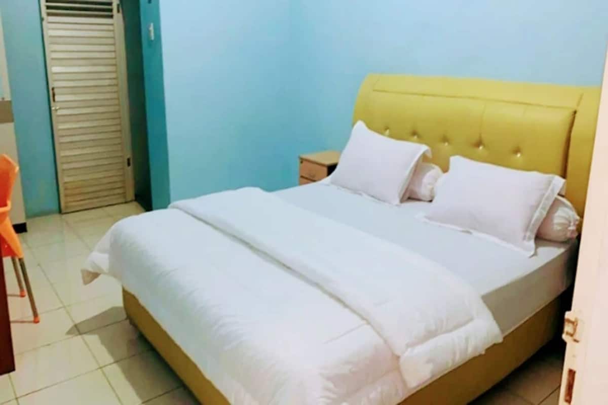 Una cama bien hecha con un cabecero amarillo y ropa de cama blanca en una habitación con paredes azul claro.