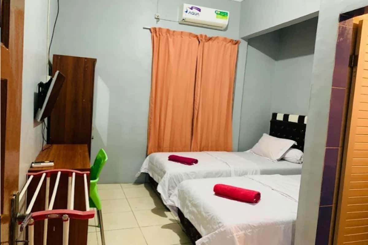 Una habitación pequeña y limpia con dos camas, un escritorio con silla y un televisor en la pared.