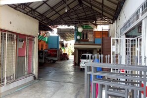 A covered parking area with a truck and a car, metal gates, and a staircase leading to a building. - Hotel O Home Stay Kembar Syariah (Binjai)