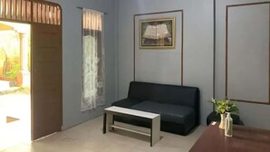 A modern living room with a dark sofa, a small white coffee table, and a wooden side table with a vase. - Hotel O Home Stay Kembar Syariah (Binjai)