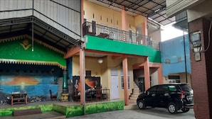 A building with a green and yellow facade, a balcony, and a parked car. - Hotel O Home Stay Kembar Syariah (Binjai)
