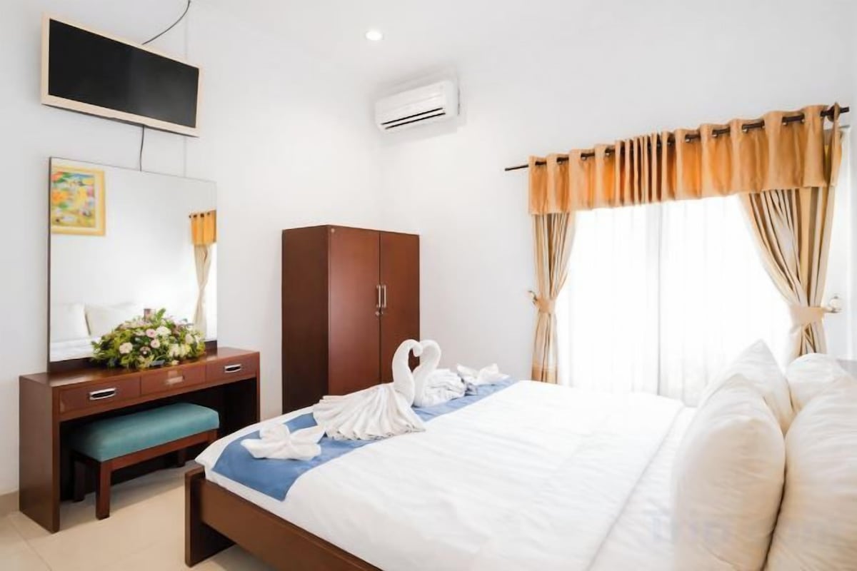 A hotel room with a bed, a desk, a wardrobe, a TV, and a window with curtains.