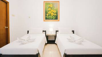 Habitación de hotel con dos camas, una mesita de noche con lámpara y un cuadro de flores en la pared.