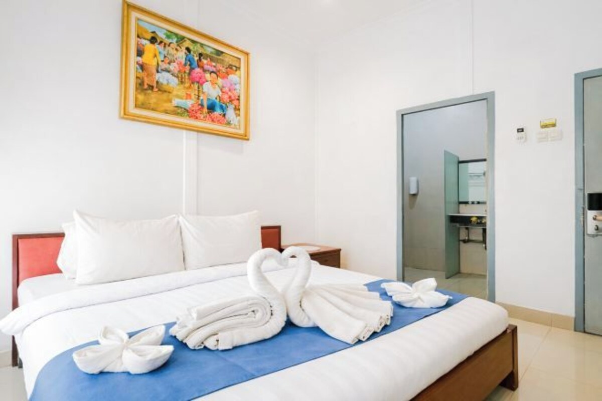 A hotel room with a bed, a painting on the wall, a mirror, and a bathroom visible through an open door.