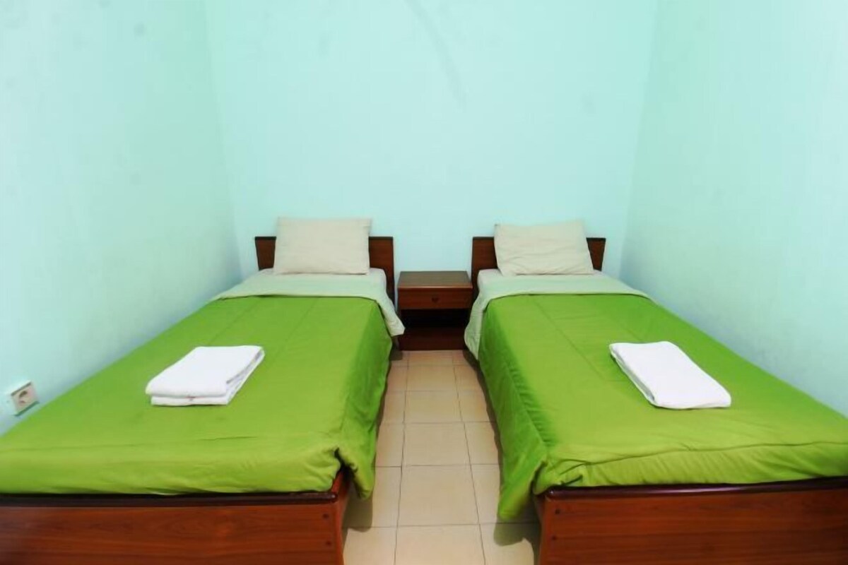 Une chambre avec deux lits simples, chacun recouvert d’une couverture verte et doté d’un oreiller blanc.