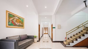 A hotel lobby with a sofa, a staircase, and a hallway leading to a door. - Tripletree Sinergi Hotel Tretes (Prigen)