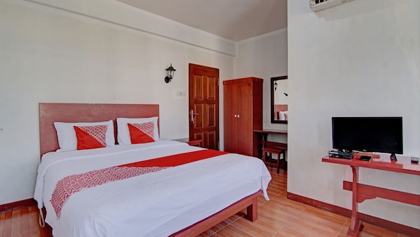 A hotel room with a bed, a TV on a stand, a wardrobe, and an air conditioning unit. - Hotel O Asri Homestay Syariah (Pekanbaru)