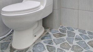 A bathroom with a white toilet, grey tiled walls, and a stone-patterned floor. - Hotel O Asri Homestay Syariah (Pekanbaru)