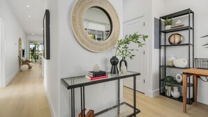 A modern living room with a glass console table, a round mirror, and a black metal shelving unit. - Golf course view - Renovated luxury 3bd in Lely, resort pool, tennis, pickleball (Naples)