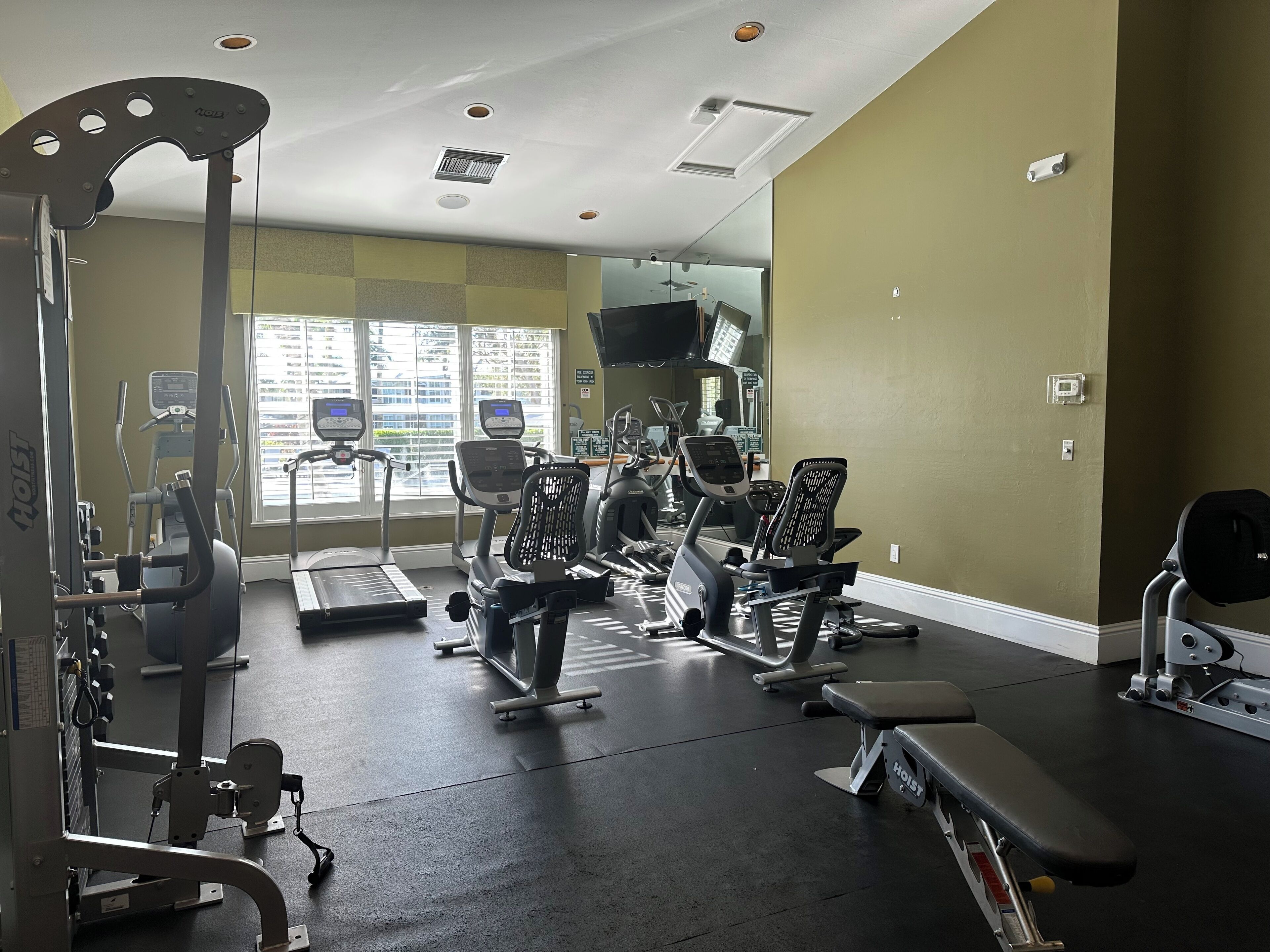 A gym with various exercise machines, a bench, and a window with a view of buildings.