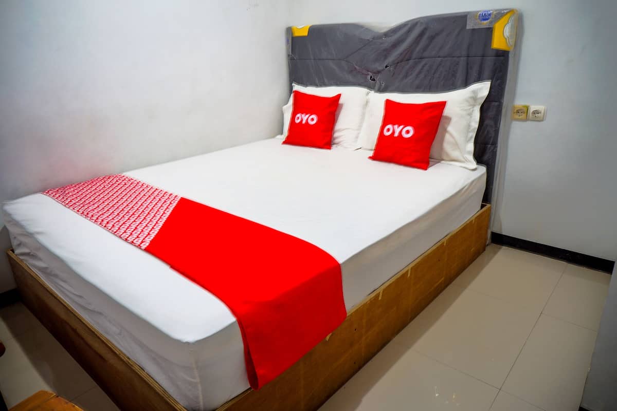 Una cama con cabecera gris, ropa de cama blanca y dos almohadas rojas con el texto "OYO".