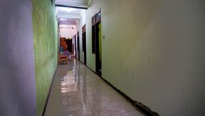 A long, narrow hallway with green and white walls, tiled floors, and doors leading to rooms. - OYO 93069 Penginapan Sumber Rizki (Sidoarjo)