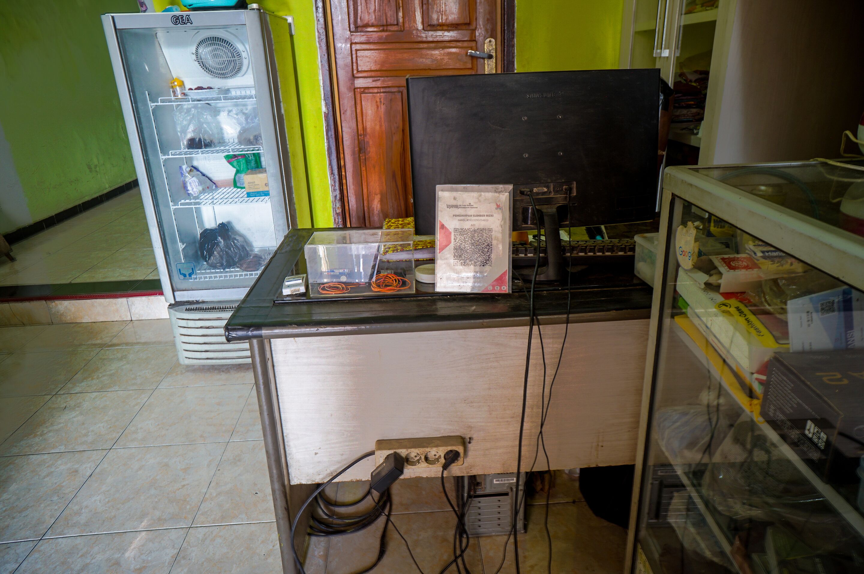 Een toonbank met een computer, een koelkast en een glazen vitrine.