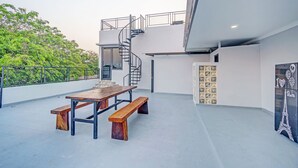 Eine moderne Terrassengestaltung im Freien mit Holztisch und -bänken, einer Wendeltreppe und Blick auf Grünflächen.