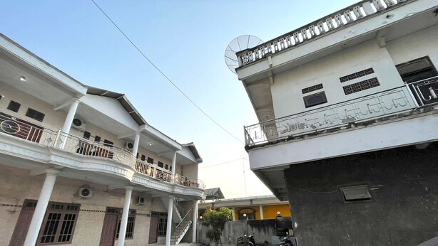 A multi-story residential building with balconies, a paved courtyard, and parked vehicles.