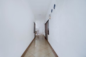 A corridor with white walls, a tiled floor, and doors leading to rooms. - OYO Life 93083 Nova Jaya 3 Homestay Syariah (Paciran)