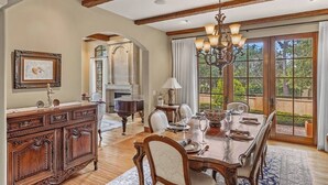 Un comedor con una mesa de madera dispuesta para seis personas, una araña y vistas a través de amplios ventanales.