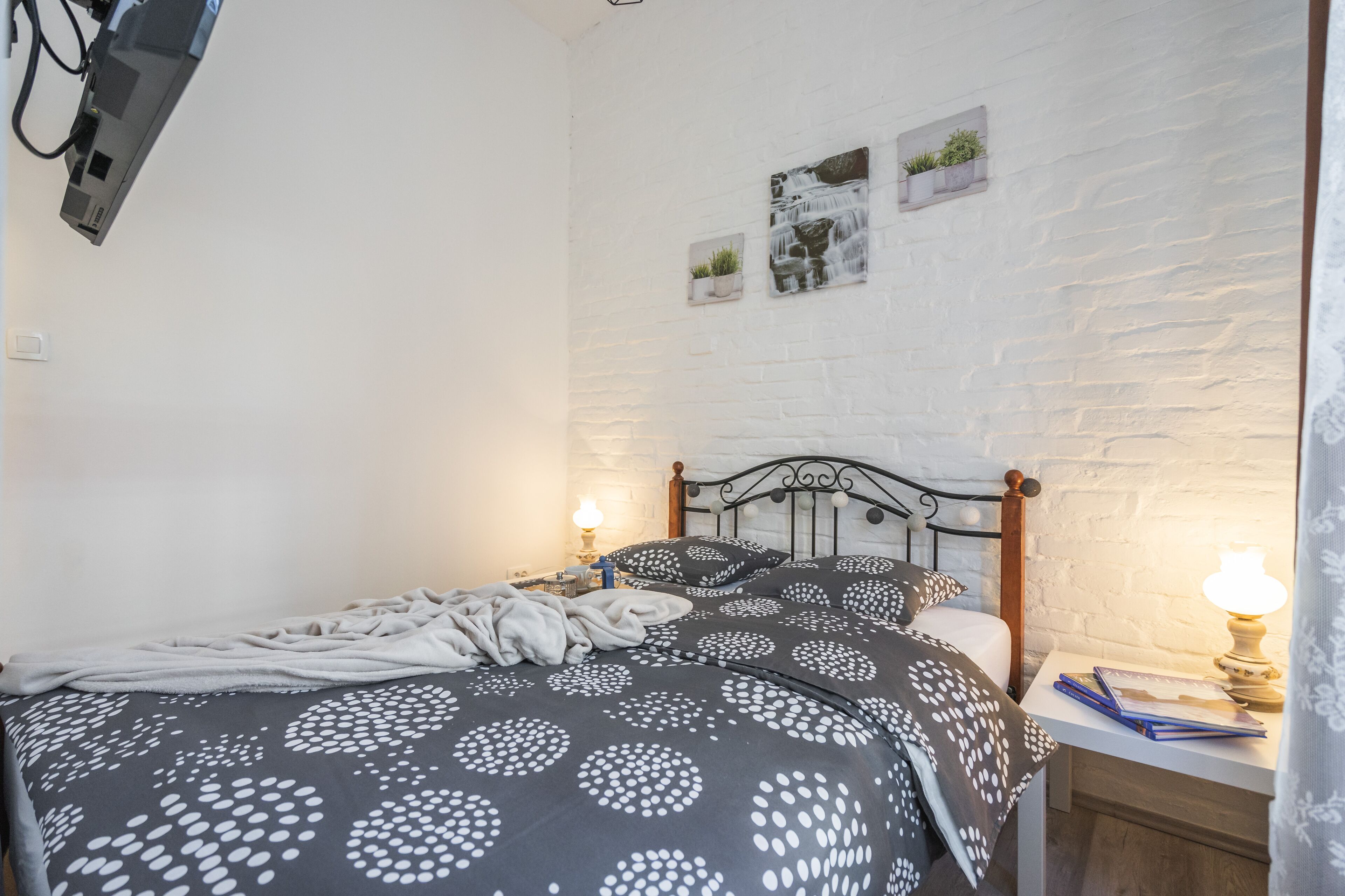 A neatly made bed with a patterned duvet, a bedside table with a lamp, and a wall-mounted TV.