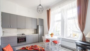 A modern kitchen with grey cabinets, a built-in oven, and a dining area with a white table and chairs. - Park Ribnjak Apartment (Zagreb)