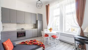 Uma cozinha moderna com armários cinza, forno embutido e área de jantar com mesa e cadeiras brancas.