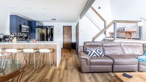 Eine moderne Küche mit Barhocker, ein Ledersofa mit einem gemusterten Kissen und ein Holztisch.