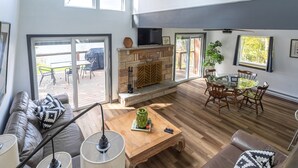 Ein modernes Wohnzimmer mit Kamin, Essbereich und einem großen Schiebeglastür, die zu einer Terrasse im Freien führt.
