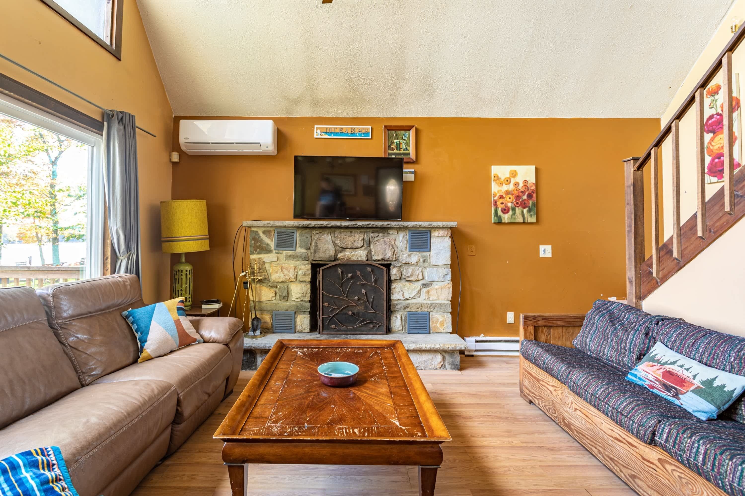 A living room with a stone fireplace, a sofa, a coffee table, and a television.