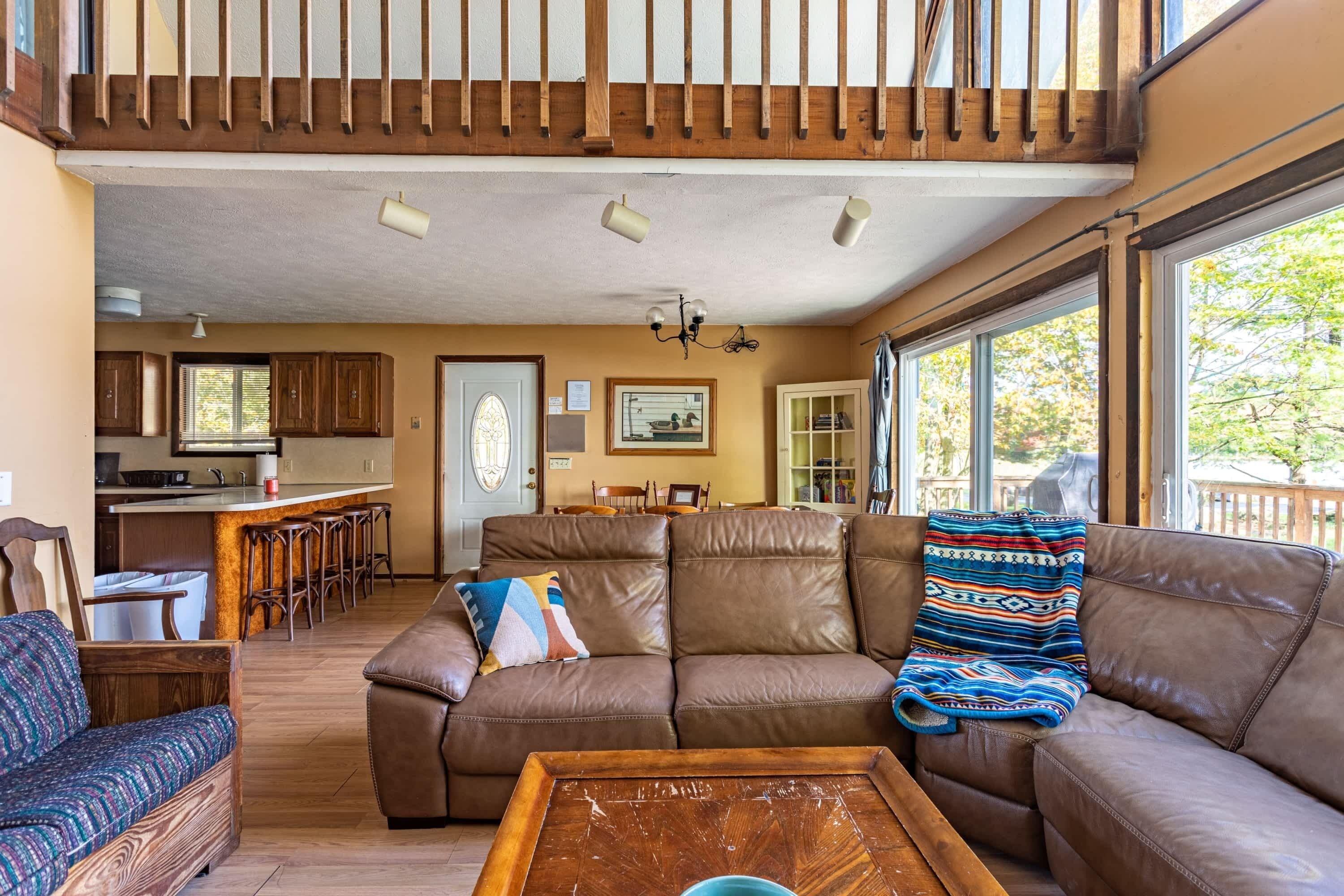 A spacious living area with a large brown leather sofa, a wooden coffee table, and a kitchen in the background.