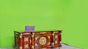 Een houten bureau met gedetailleerde houtsnijwerken, met daarop een laptop, tegen een groene muur.
