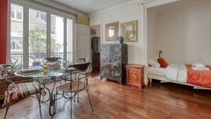 Quarto com cama, mesa de jantar com cadeiras, armário e janela com vista para edifícios.
