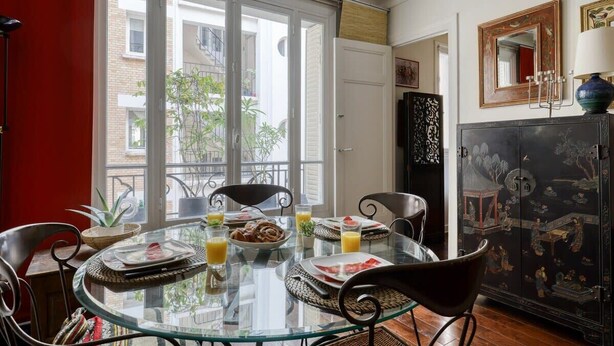 Uma sala de jantar com mesa de vidro, cadeiras e um buffet com pratos e copos.