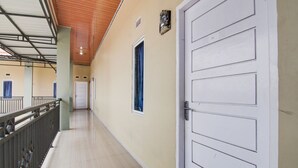 A corridor with a white door, a window with blue curtains, and a metal railing. - OYO 93087 Wisma Apel Syariah (Pekanbaru)