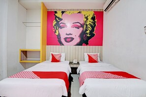 A hotel room with two beds, each with red and white bedding, a small bedside table with a phone, and a large pop art mural on the wall. - Hotel O Celine Home Syariah (Pekanbaru)