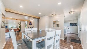A modern dining area with a wooden table and white chairs, a kitchen in the background, and a hallway leading to other rooms. - Sleeps 20 * 4,400 Sq Ft * Indoor Heated Pool (Brillion)