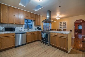 A kitchen with wooden cabinets, a stainless steel dishwasher, a stove, and a window with curtains. - Sam Hughes Retreat by Velo (Tucson)