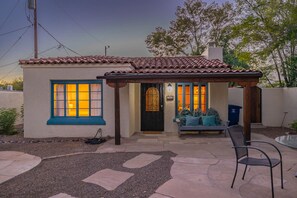 A small house with a tiled roof, a porch with a bench, and a patio area with a chair. - Sam Hughes Retreat by Velo (Tucson)